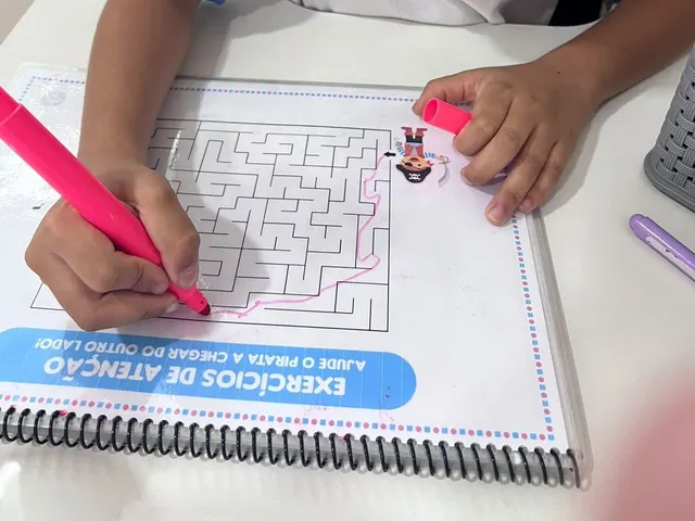 Mão de uma criança fazendo um labirinto num caderno de exercícios de atenção